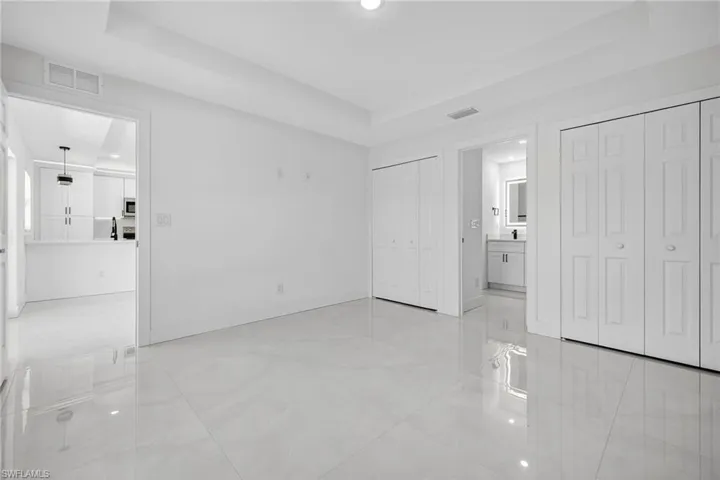 Unfurnished bedroom featuring a raised ceiling, multiple closets, light tile patterned flooring, ensuite bath, and recessed lighting