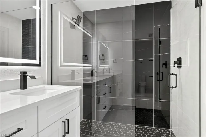 Bathroom featuring two vanities, dark tile patterned flooring, and a stall shower