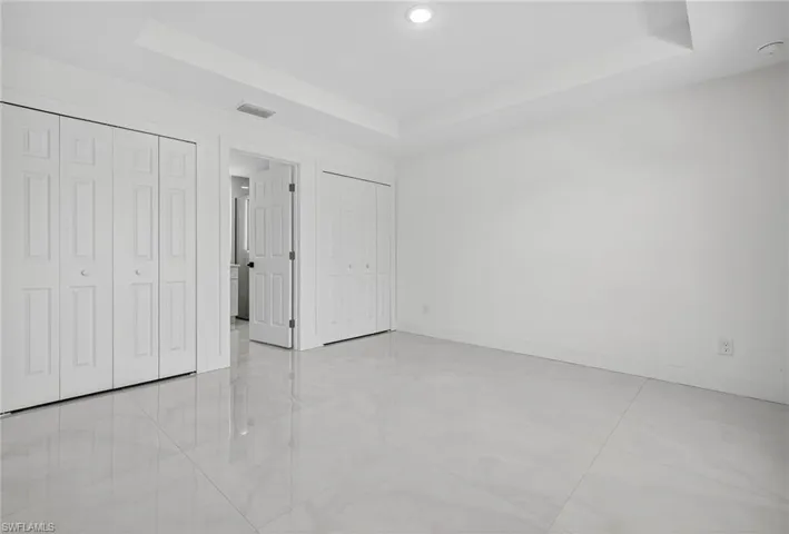 Unfurnished bedroom featuring a raised ceiling, multiple closets, and light tile patterned floors