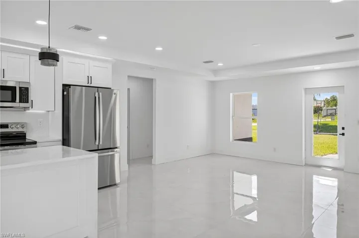Kitchen with stainless steel appliances, light stone counters, white cabinetry, recessed lighting, and pendant lighting