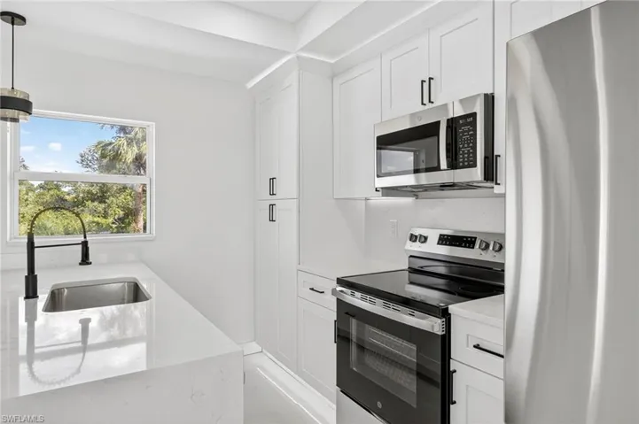 Kitchen with stainless steel appliances, white cabinetry, light stone countertops, and pendant lighting