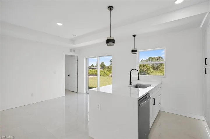 Kitchen with white cabinets, light stone counters, a peninsula, decorative light fixtures, and plenty of natural light
