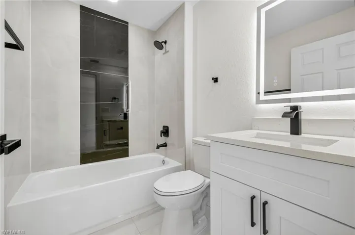 Bathroom with vanity, washtub / shower combination, a textured wall, and tile patterned floors