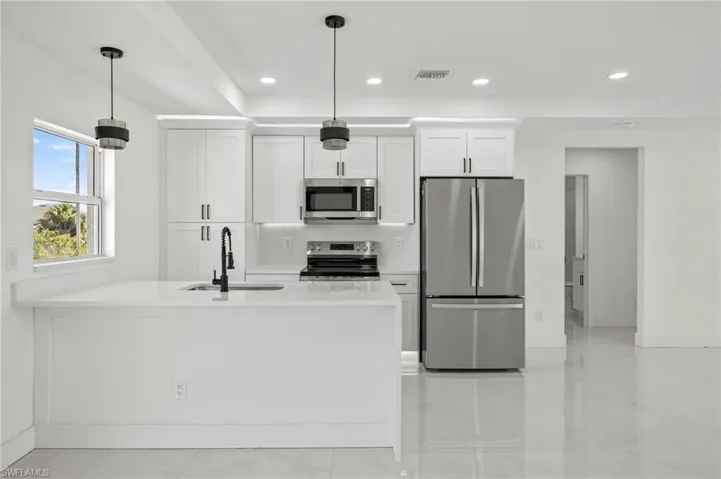 Kitchen featuring stainless steel appliances, a peninsula, white cabinets, light stone countertops, and recessed lighting