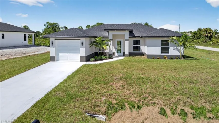 Prairie-style home with stucco siding, driveway, a front lawn, an attached garage, and a shingled roof