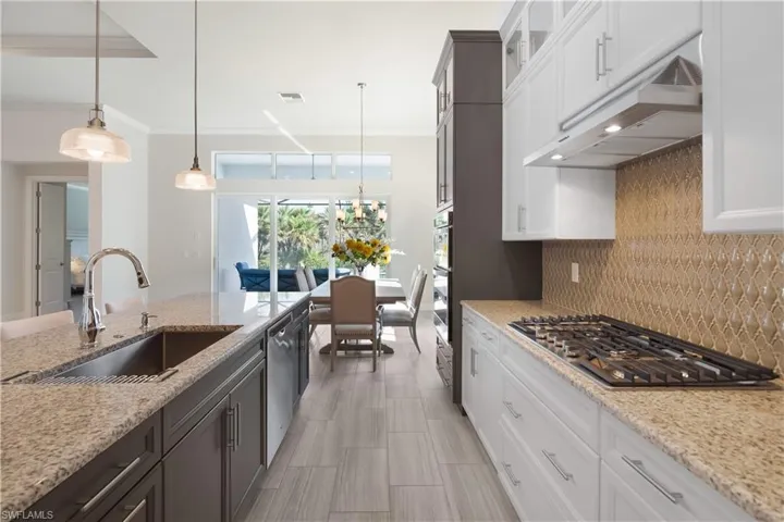 Kitchen with hanging light fixtures, white cabinets, decorative backsplash, light stone countertops, and appliances with stainless steel finishes