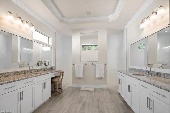 Full bathroom featuring two vanities, ornamental molding, and a tray ceiling