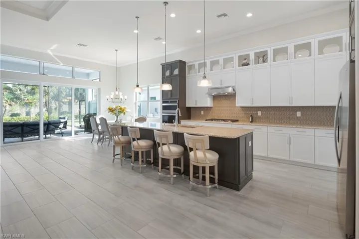Kitchen featuring a kitchen bar, white cabinets, decorative light fixtures, light stone countertops, and crown molding