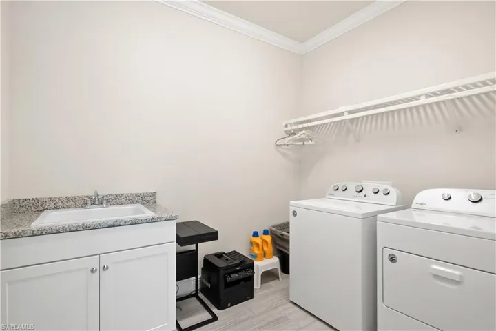 Laundry area featuring crown molding, separate washer and dryer, cabinet space, and light wood-type flooring