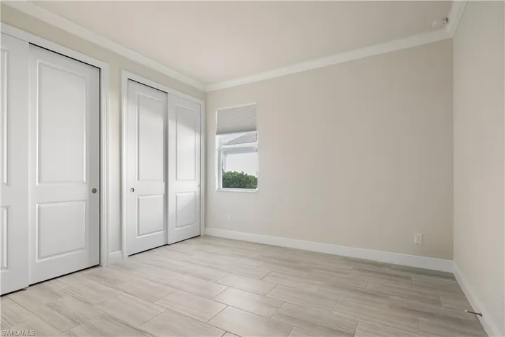 Unfurnished bedroom with ornamental molding, multiple closets, and wood finish floors