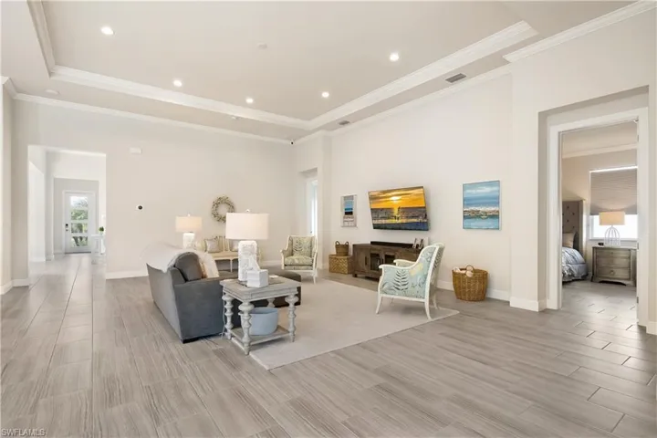 Living room with wood finish floors, recessed lighting, a raised ceiling, and ornamental molding