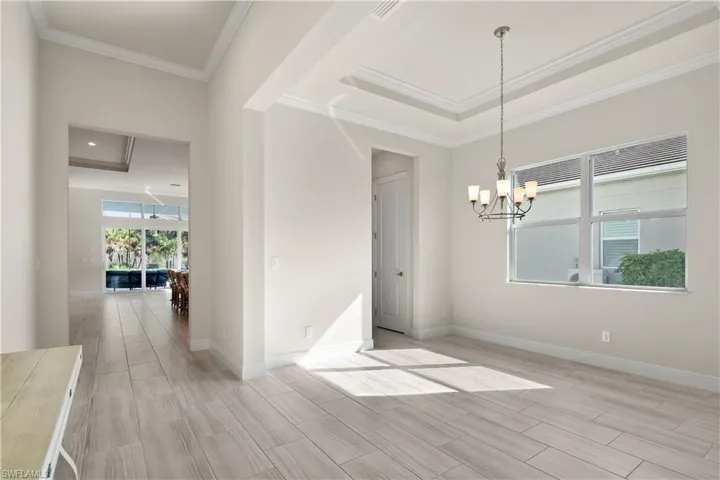 Unfurnished dining area with a tray ceiling, a chandelier, wood finish floors, and ornamental molding