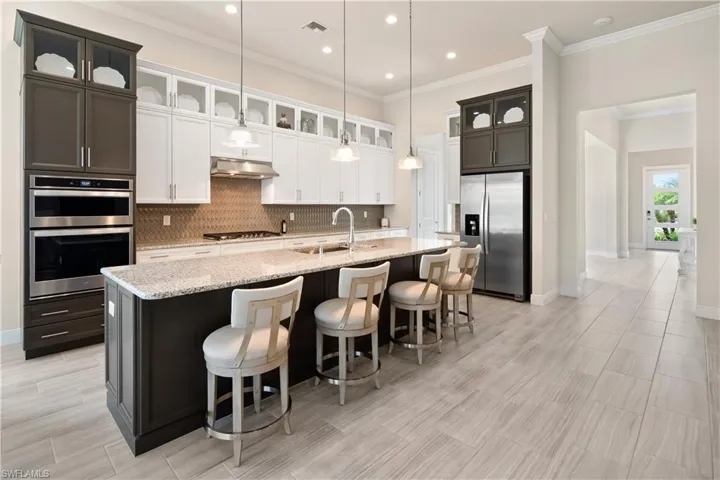 Kitchen with glass insert cabinets, light stone counters, appliances with stainless steel finishes, a kitchen breakfast bar, and crown molding