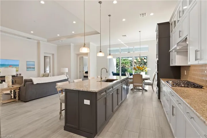 Kitchen featuring white cabinets, open floor plan, a breakfast bar area, light stone countertops, and decorative light fixtures
