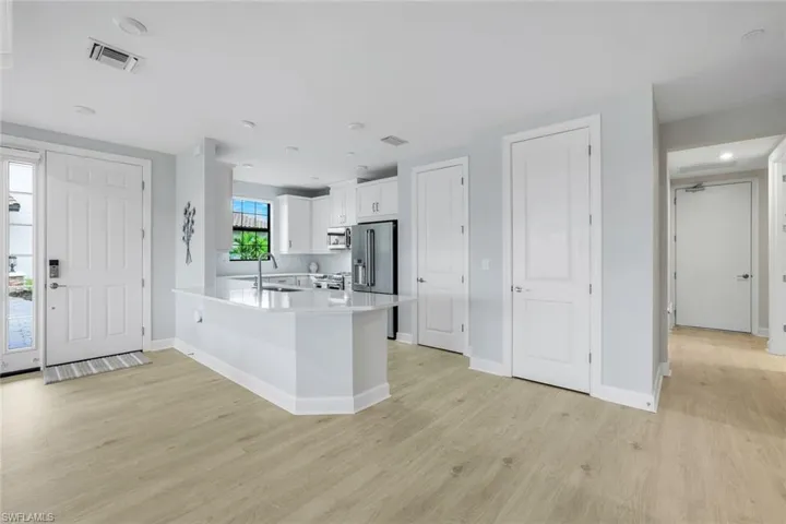 Kitchen with white cabinetry, a peninsula, appliances with stainless steel finishes, light wood-type flooring, and a kitchen bar
