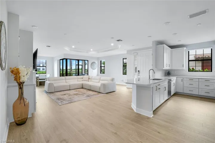 Kitchen with white cabinets, a peninsula, light wood finished floors, light stone countertops, and a tray ceiling