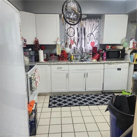 Kitchen featuring white cabinetry, light-toned countertops, a double basin sink, and a built-in dishwasher