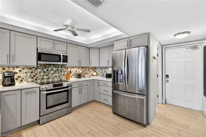 Kitchen featuring gray cabinets, appliances with stainless steel finishes, a tray ceiling, and wood finish floors