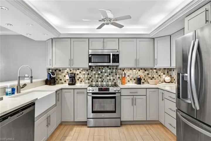 Kitchen featuring stainless steel appliances, gray cabinetry, light stone countertops, crown molding, and light wood-type flooring
