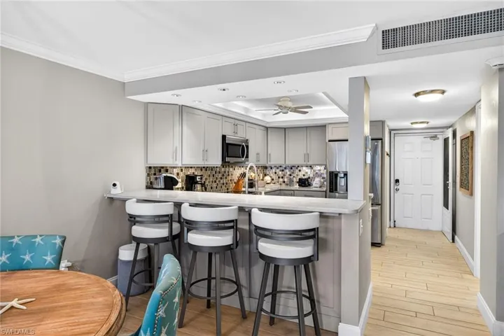 Kitchen featuring a kitchen breakfast bar, light countertops, gray cabinets, tasteful backsplash, and light wood-style floors