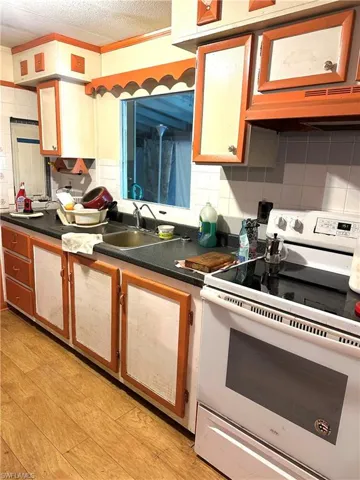 Kitchen with white range with electric stovetop, backsplash, under cabinet range hood, dark countertops, and a sink
