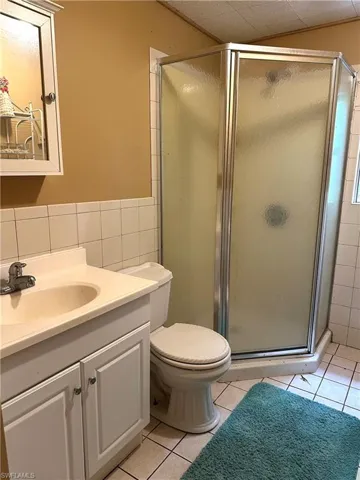 Full bath with tile walls, a stall shower, tile patterned flooring, vanity, and wainscoting