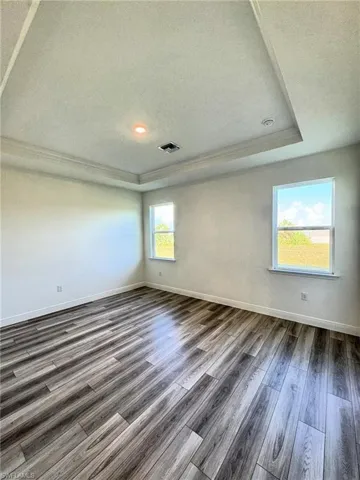 Empty room with ornamental molding, a tray ceiling, dark wood-style floors, baseboards, and a textured ceiling