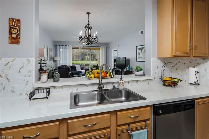 Kitchen with tasteful backsplash, stainless steel dishwasher, light countertops, a chandelier, and wood finish cabinetry