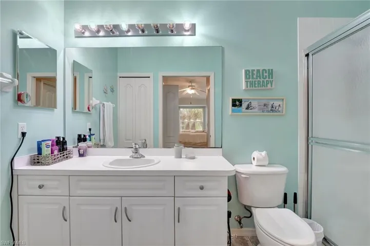 Bathroom with a shower with shower door, vanity, ceiling fan, and toilet