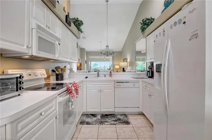 Kitchen with white cabinetry, hanging light fixtures, white appliances, and light tile patterned floors