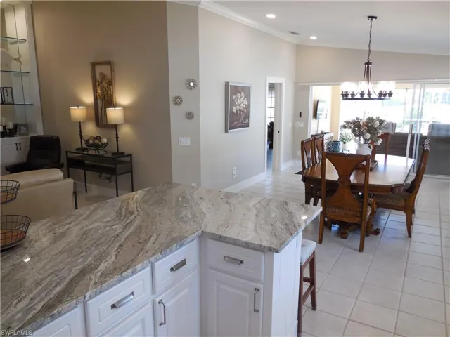 Kitchen featuring light stone counters, a chandelier, light tile patterned floors, white cabinets, and ornamental molding