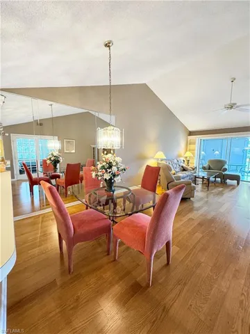 Dining area with lofted ceiling, wood-type flooring, ceiling fan with notable chandelier, and a textured ceiling