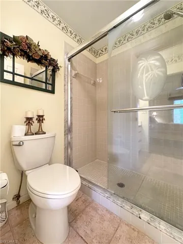 Bathroom with an enclosed shower, toilet, and tile patterned flooring