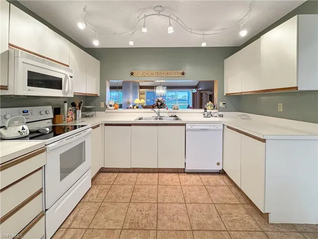 Kitchen with sink, white appliances, white cabinetry, light tile patterned floors, and rail lighting