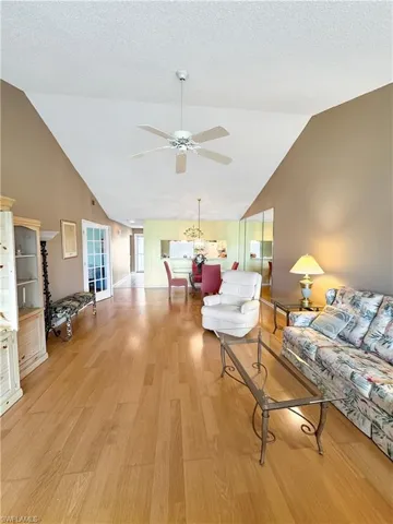 Living room featuring vaulted ceiling, a textured ceiling, ceiling fan with notable chandelier, and light hardwood / wood-style flooring