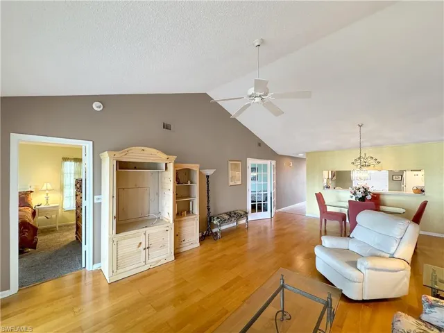 Living room with ceiling fan with notable chandelier, wood-type flooring, lofted ceiling, and a textured ceiling