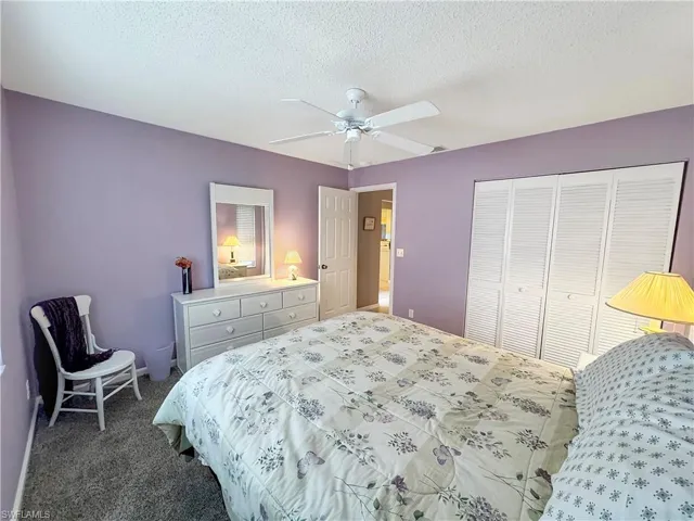 Carpeted bedroom with ceiling fan, a closet, and a textured ceiling
