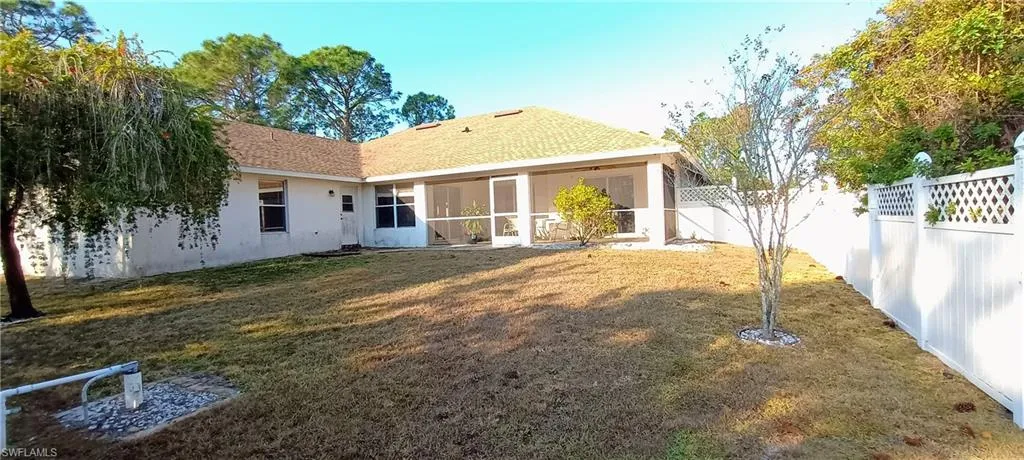 Back of property with a sunroom, a shingled roof, stucco siding, and a fenced backyard