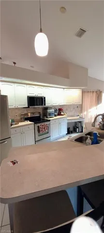Kitchen with stainless steel appliances, light countertops, backsplash, hanging light fixtures, and white cabinetry