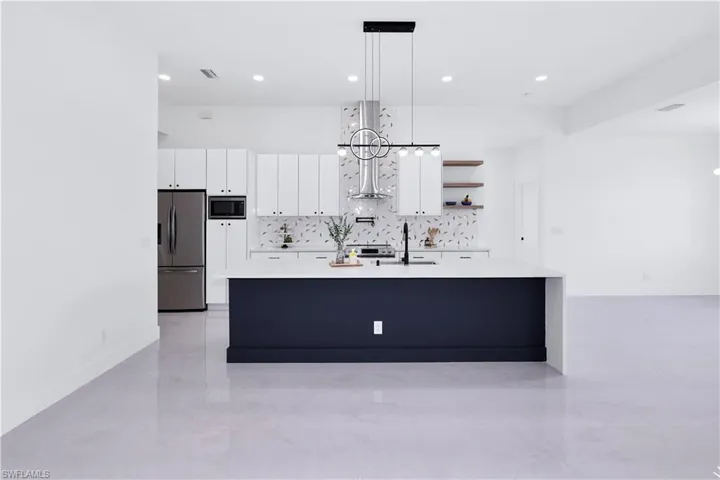 Kitchen with sink, backsplash, pendant lighting, appliances with stainless steel finishes, and white cabinetry