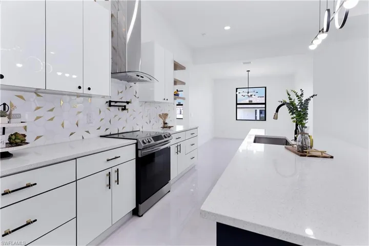 Kitchen featuring white cabinetry, sink, wall chimney exhaust hood, stainless steel range with electric cooktop, and decorative light fixtures