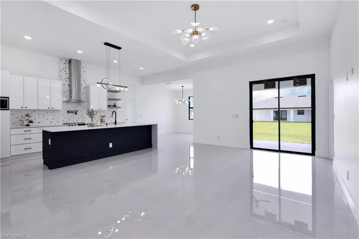 Kitchen with white cabinetry, backsplash, wall chimney range hood, an inviting chandelier, and a kitchen island with sink