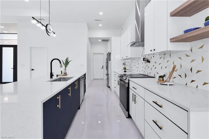 Kitchen with white cabinetry, appliances with stainless steel finishes, wall chimney exhaust hood, and sink