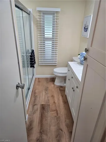 Bathroom with vanity, wood-type flooring, a shower with shower door, and toilet