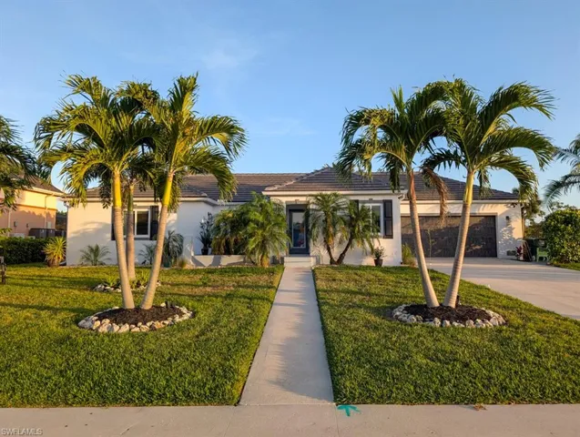 Ranch-style house featuring a tile roof, stucco siding, an attached garage, driveway, and a front lawn