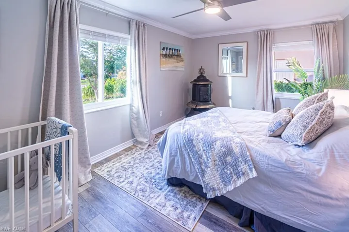 Bedroom with baseboards, ornamental molding, wood finished floors, ceiling fan, and a wood stove