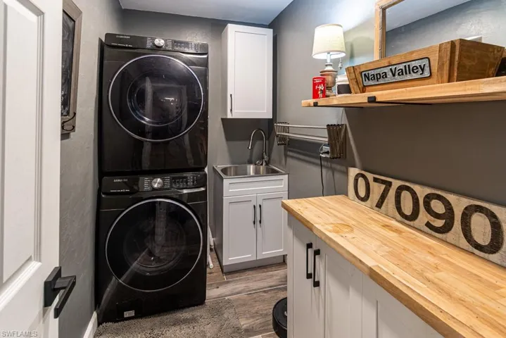 Washroom with a sink, cabinet space, dark wood-style floors, and stacked washer / drying machine