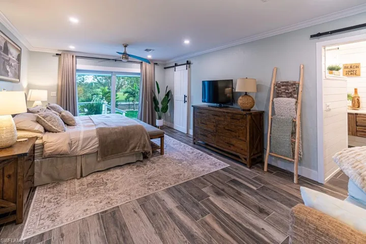 Bedroom with baseboards, dark wood-style floors, a barn door, and crown molding