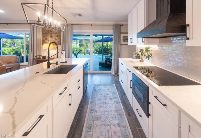Kitchen featuring dishwasher, dark wood finished floors, a sink, black electric stovetop, and exhaust hood