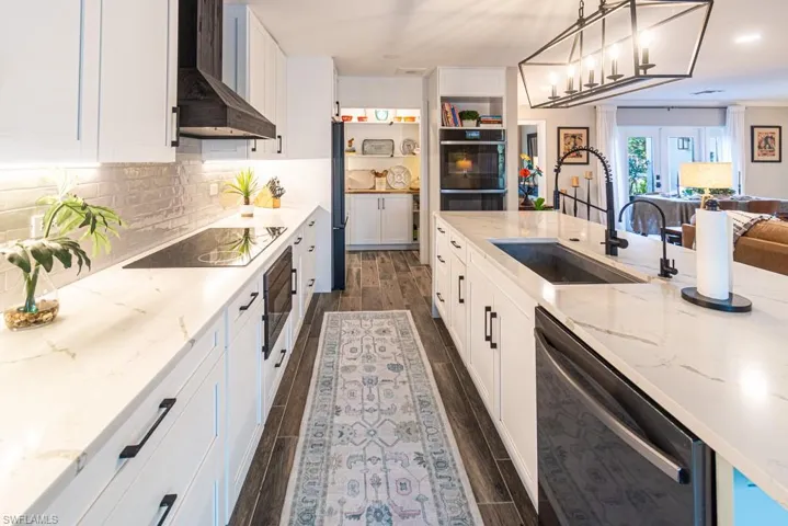 Kitchen featuring open floor plan, wood finish floors, a sink, wall chimney range hood, and black appliances